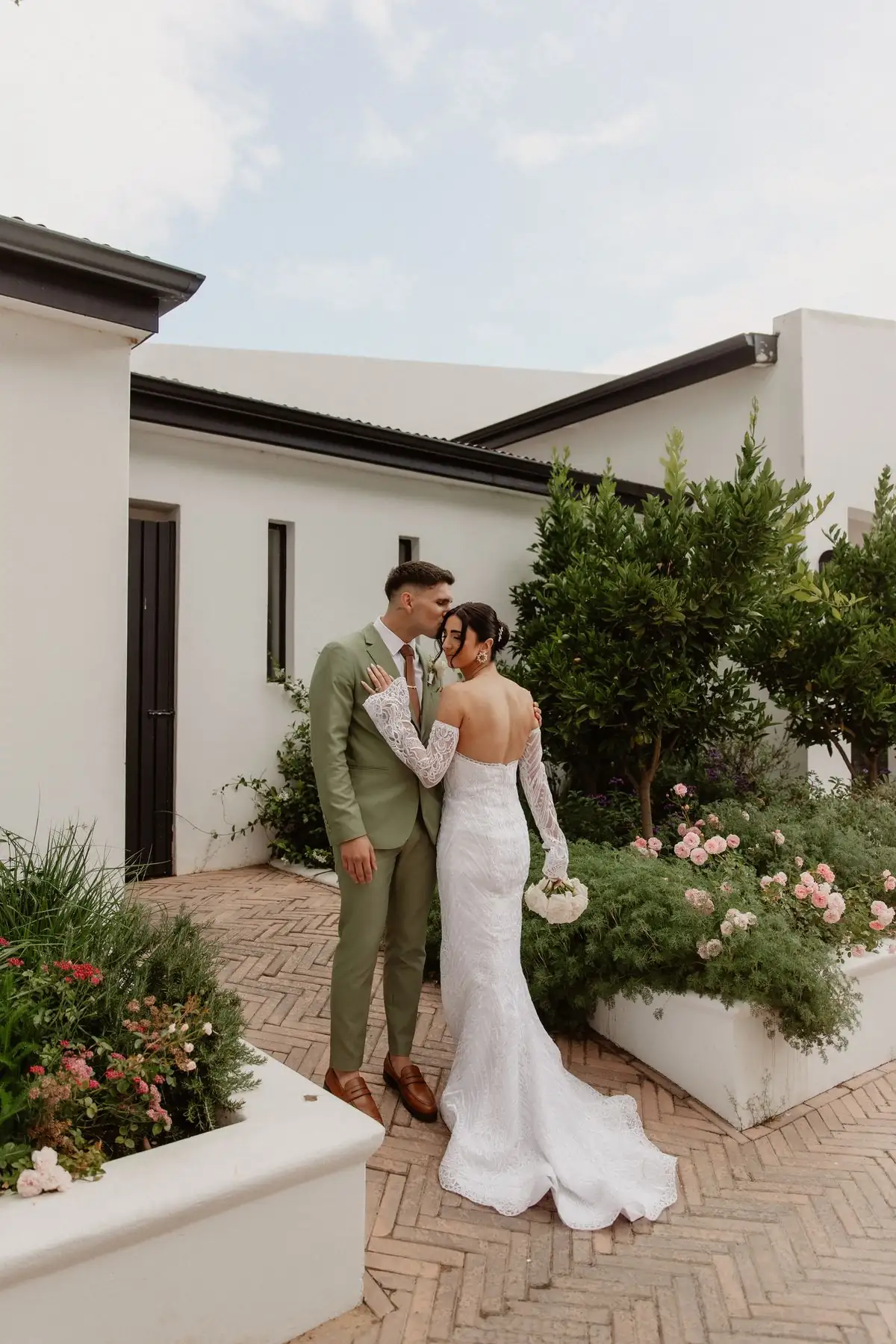A couple close together in a courtyard of white walls and flowers