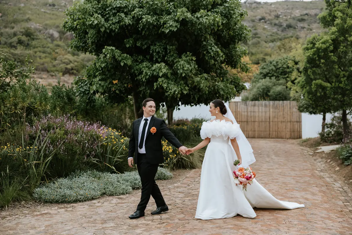 A bride and groom walking along the farm road, the mountain behind them