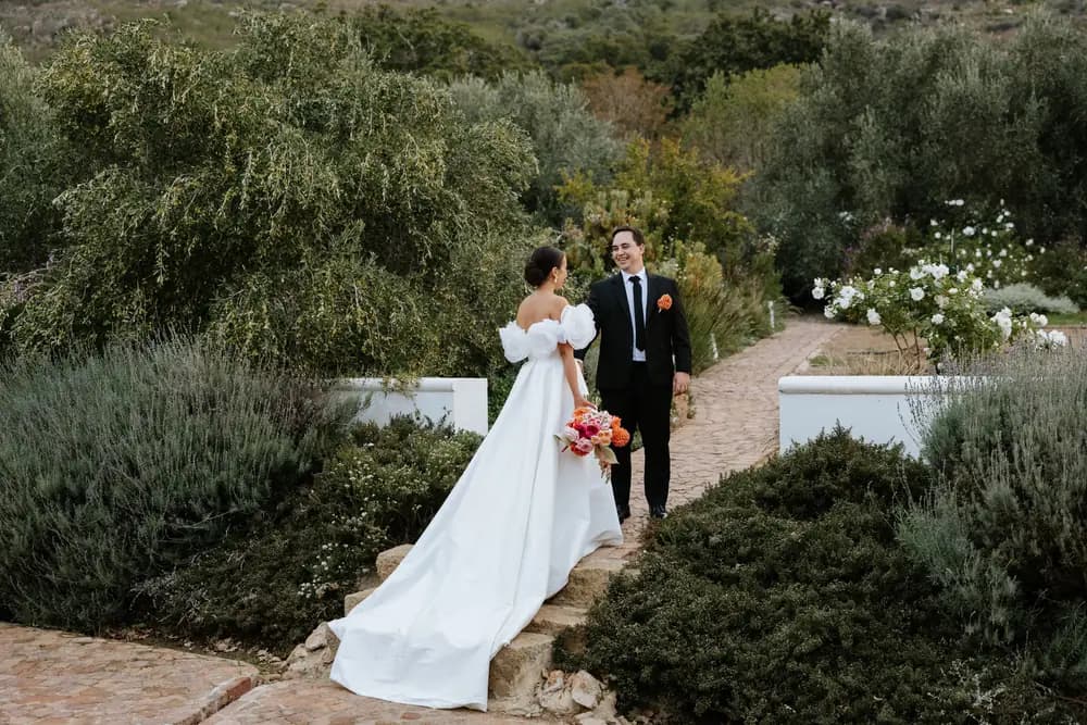 A groom leading his bride up garden steps, her bouquet in hand