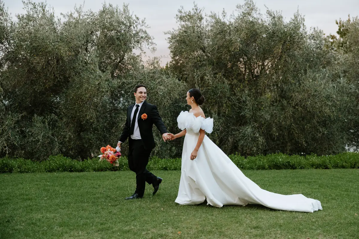 A bride and groom walking hand in hand across the lawn, her train behind her