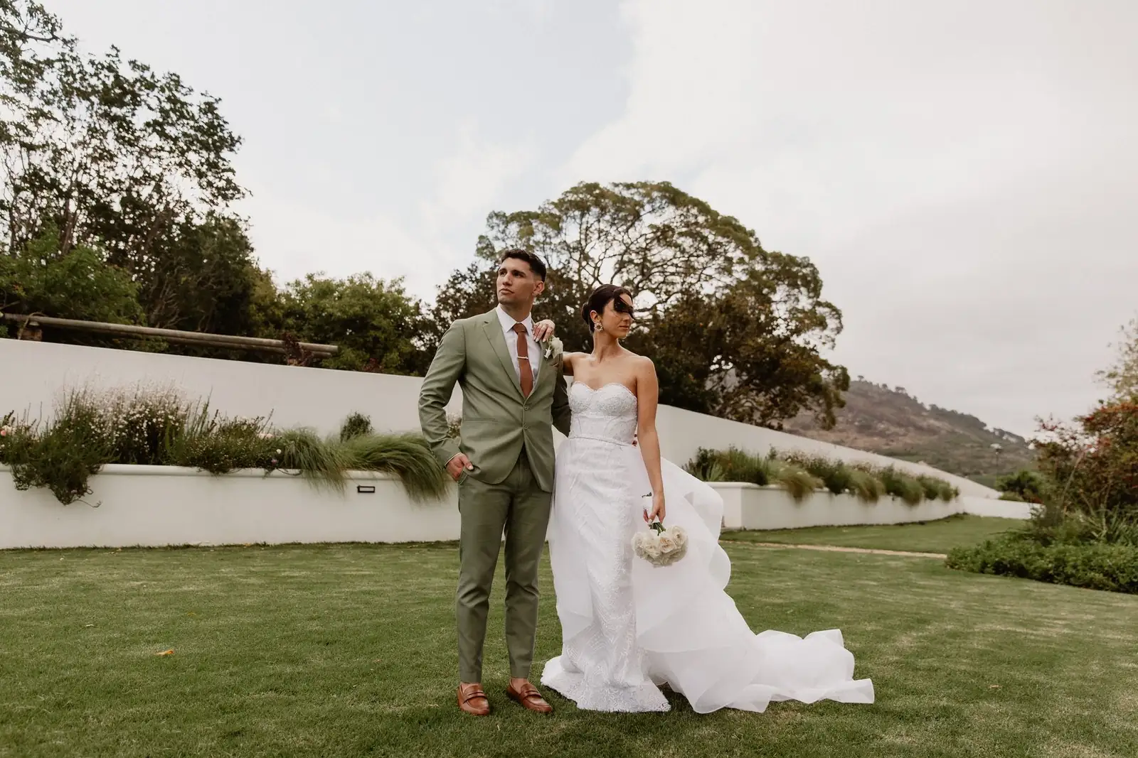 A bride and groom on the lawn, her dress caught by the breeze