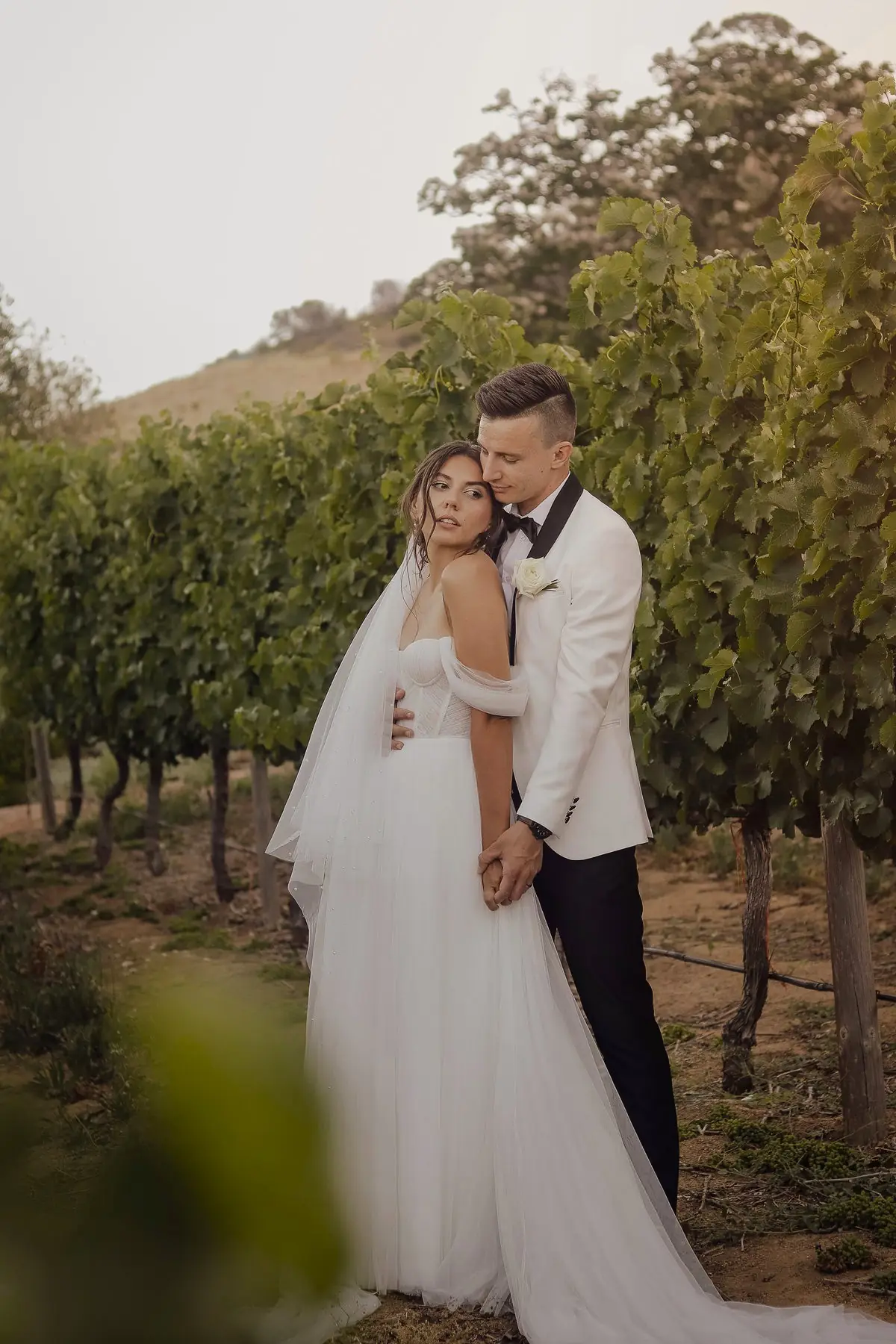 A groom holding his bride close among the vines