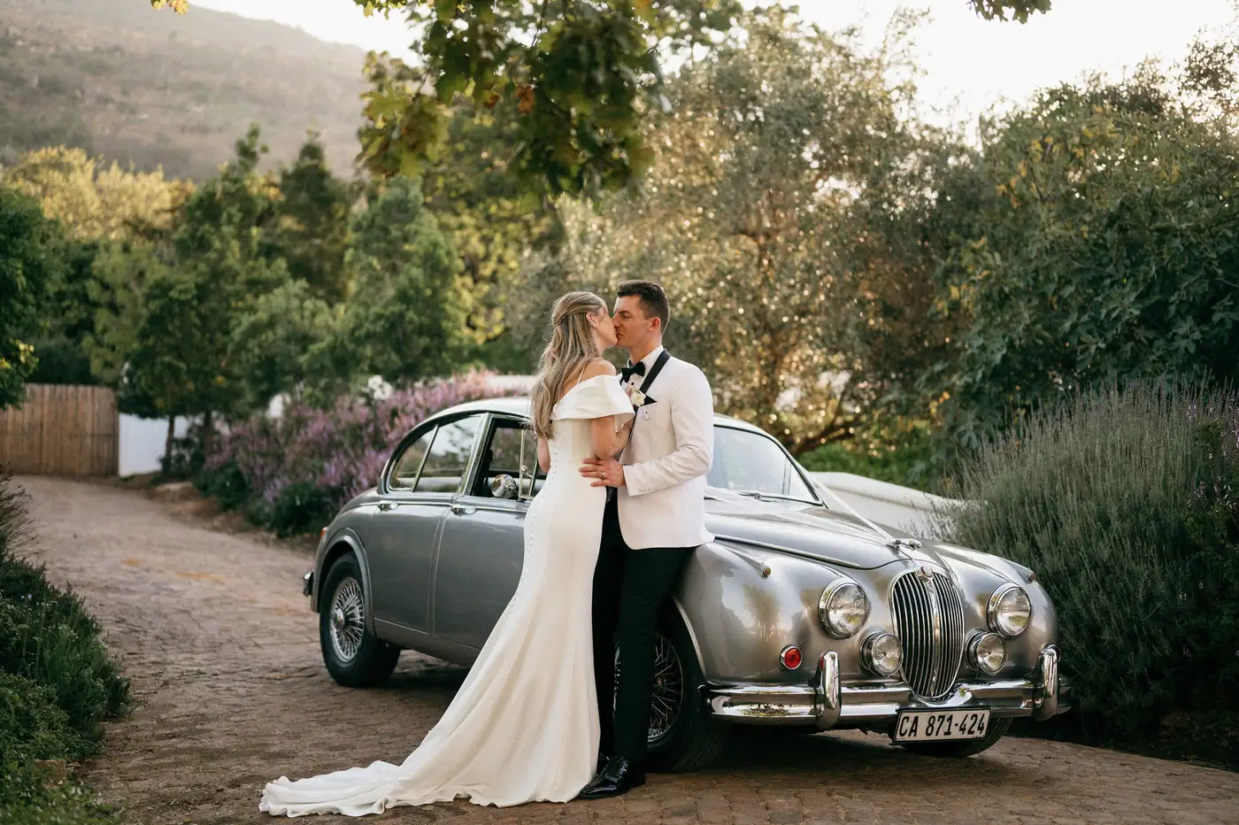 A couple kissing beside a silver vintage car on the farm road