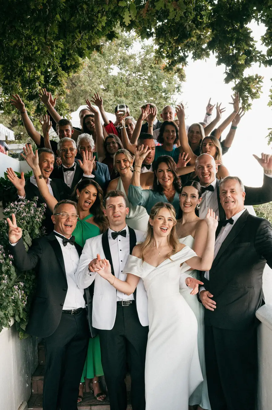 A bride and groom with their guests crowded around, arms raised and cheering