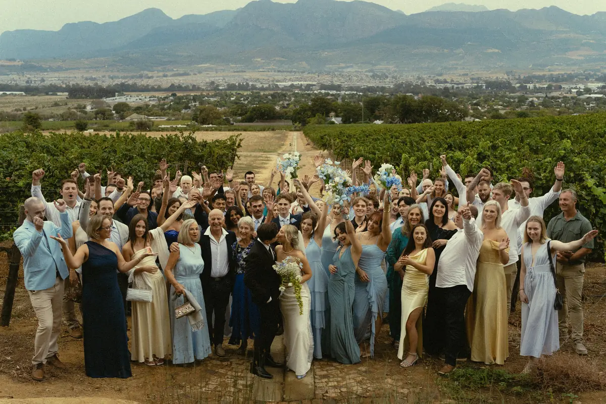 A large wedding party cheering in the vineyards, the valley and mountains beyond